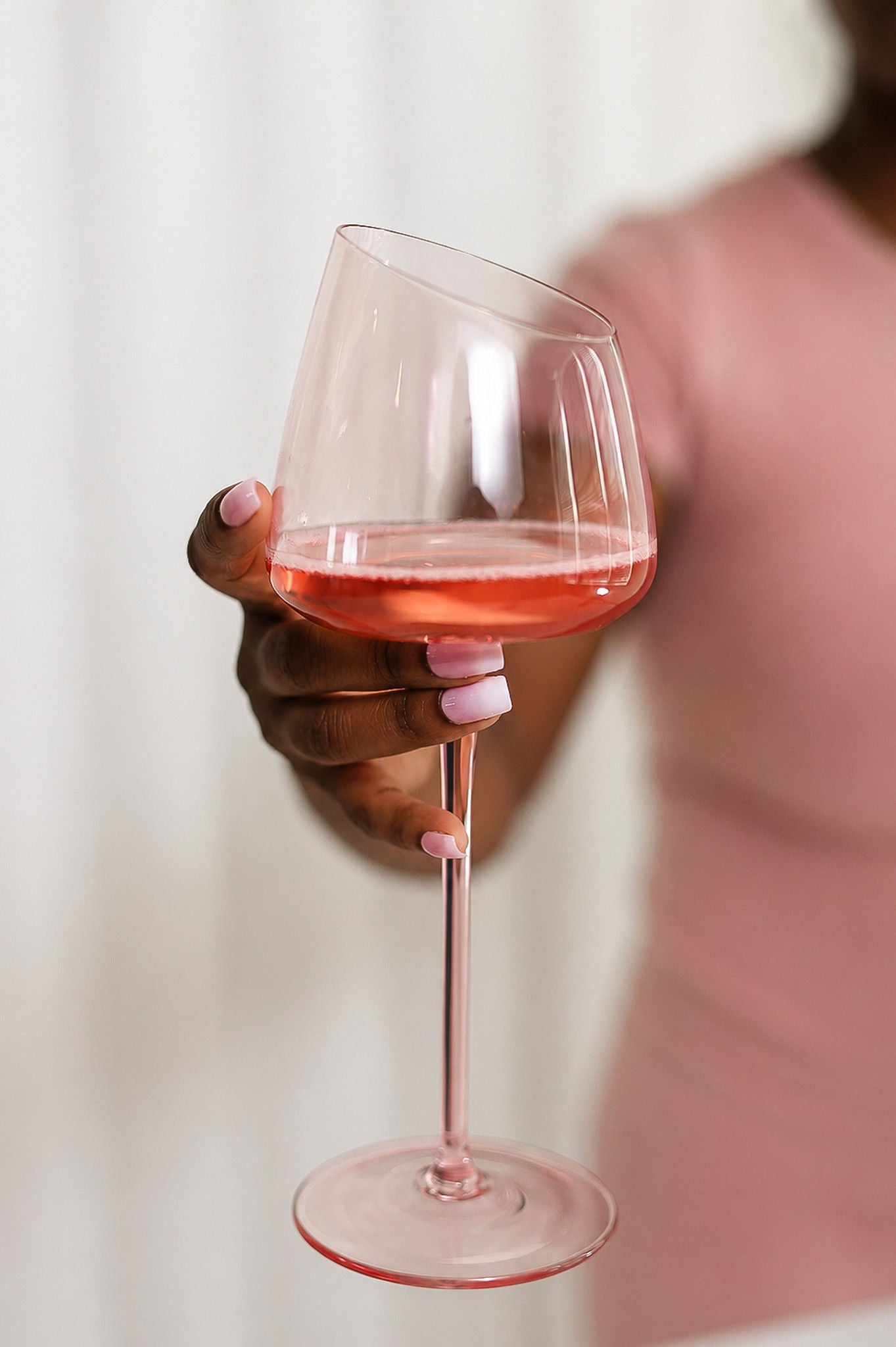 Hand holding a glass of pink wine against a blurred background